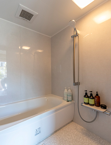 浴室にガラス戸を採用したことで、バルコニー越しに街路樹の緑を楽しめるようになったＮ様邸。浴室も洗面所も、白を基調にシルバーのパーツを組み合わせ、非日常的な時間を味わえる空間です。システムバス「マンションリモデルWYシリーズ」（TOTO）を採用